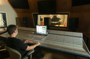 An audio engineer operating a digital audio mixing board is shown in this provided photo.