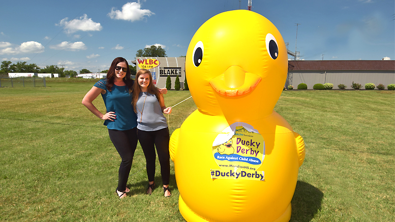 Lindsay Stafford and Liz Valpatic beside one of the 8 foot yellow ducks on the property of Woof Boom Radio. Photo by: Mike Rhodes