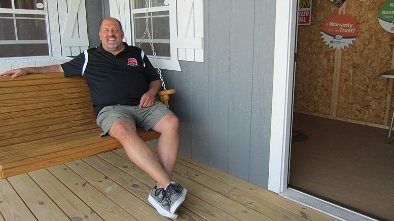 Scott Quirk, owner of The Barn Lot, relaxes on the porch swing of a tiny house. Photo by: John Carlson