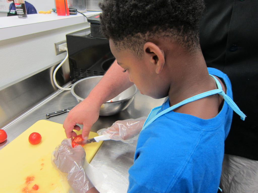 With a little help, a young chef safely slices a tomato. Photo by: John Carlson