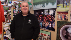 Al Holdren is pictured standing beside hundreds of photos of thousands of volunteers who participate in "Secret Families." Photo by Mike Rhodes.