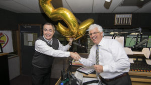 J Chapman, president of Woof Boom Radio, congratulates Steve Lindell for his 25 years of service at WLBC. Two rather unwieldy balloons, (a "2" and a "5") are also pictured. Photo by: Mike Rhodes