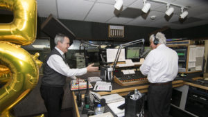 J Chapman, president of Woof Boom Radio, congratulates Steve Lindell for his 25 years of service at WLBC. Two rather unwieldy balloons, (a "2" and a "5") are also pictured. Photo by: Mike Rhodes