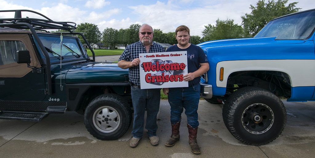 Troy Watters and son Nick Watters are pictured by their favorite Jeep and '79 GMC High Sierra Square Body truck. The sign they are holding appears by South Madison Street businesses who encourage participants to pull into their parking lots. Photo by: Mike Rhodes