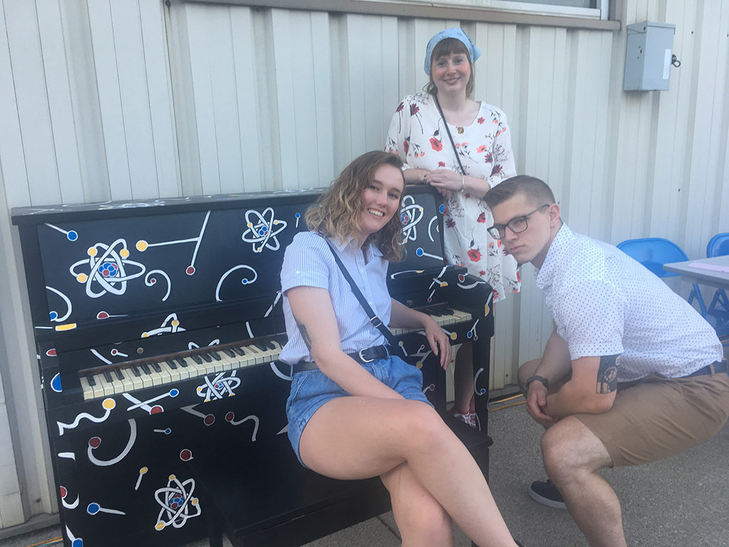 Sarah Vise, Maggie Weeks-Foy, and Quinn Hurley pose in front of the piano they painted together. The piano art was designed by Vise, a recent Ball State University graduate with degrees in physics and astronomy. Photo provided