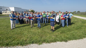 Community leaders, local officials, and Magna Powertrain leadership are pictured during ribbon-cutting ceremonies held today. Pictured holding the scissors for the ribbon-cutting are Stephen Brand, Magna Powertrain General Manager and Joe Barr, Assistant General Manager. The walking track for employees can be seen winding around the property. Photo by: Mike Rhodes