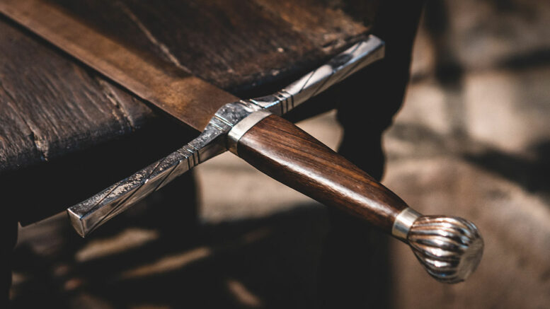 A metal sword lays on a brown table. Photo by Jonathan Kemper on Unsplash