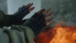 A homeless man with fingerless gloves, stands beside a fire pit in an attempt to get warm. Photo by Storyblocks.