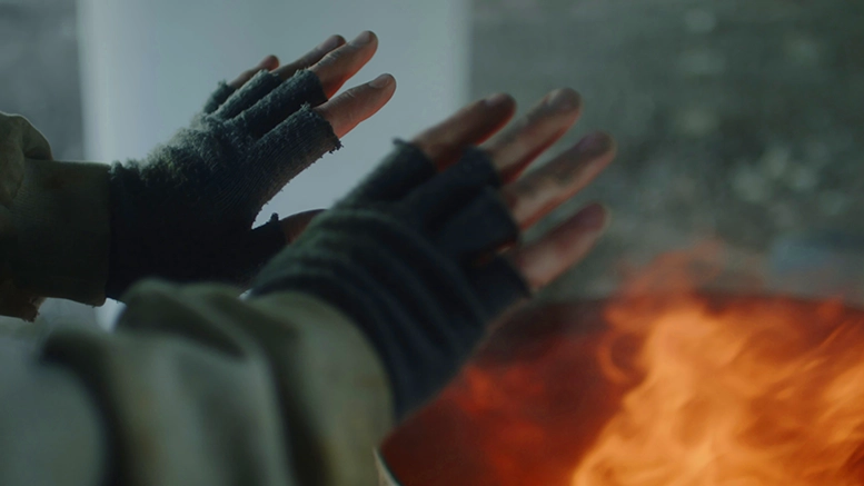 A homeless man with fingerless gloves, stands beside a fire pit in an attempt to get warm. Photo by Storyblocks.