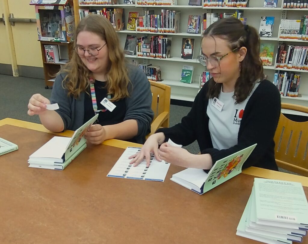 Kays Keesling and Hannah Simon, MPL Information Services Specialists, help put stickers in books in preparation of the Big Read Kick Off event. Photo by Spenser Query, MPL Webmaster & Social Media Specialist.